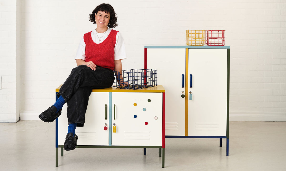 Becca seated on The Lowdown locker beside The Midi, styled with wire Baskets and Buttons in the Mustard x MoMA palette