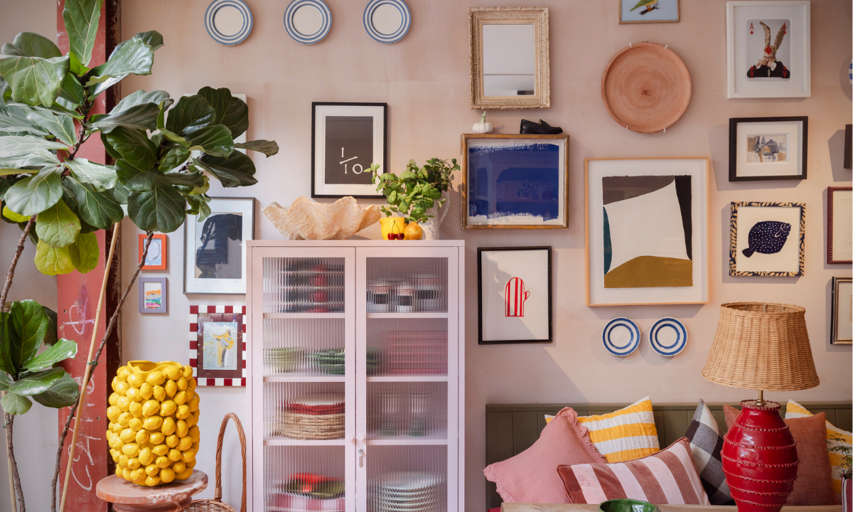 A Blush pink locker with glass doors against a pink wall filled with an eclectic mix of framed artworks, plants, cushions and other decor items.