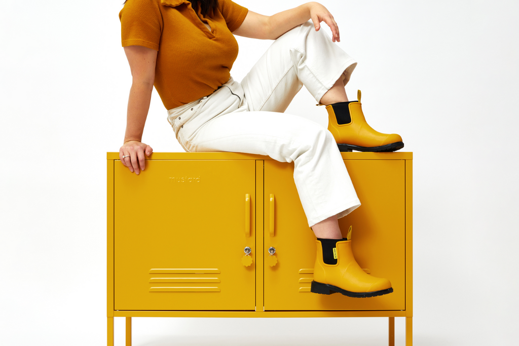 Becca sitting on top of The Lowdown Locker in Mustard, wearing Merry People boots.