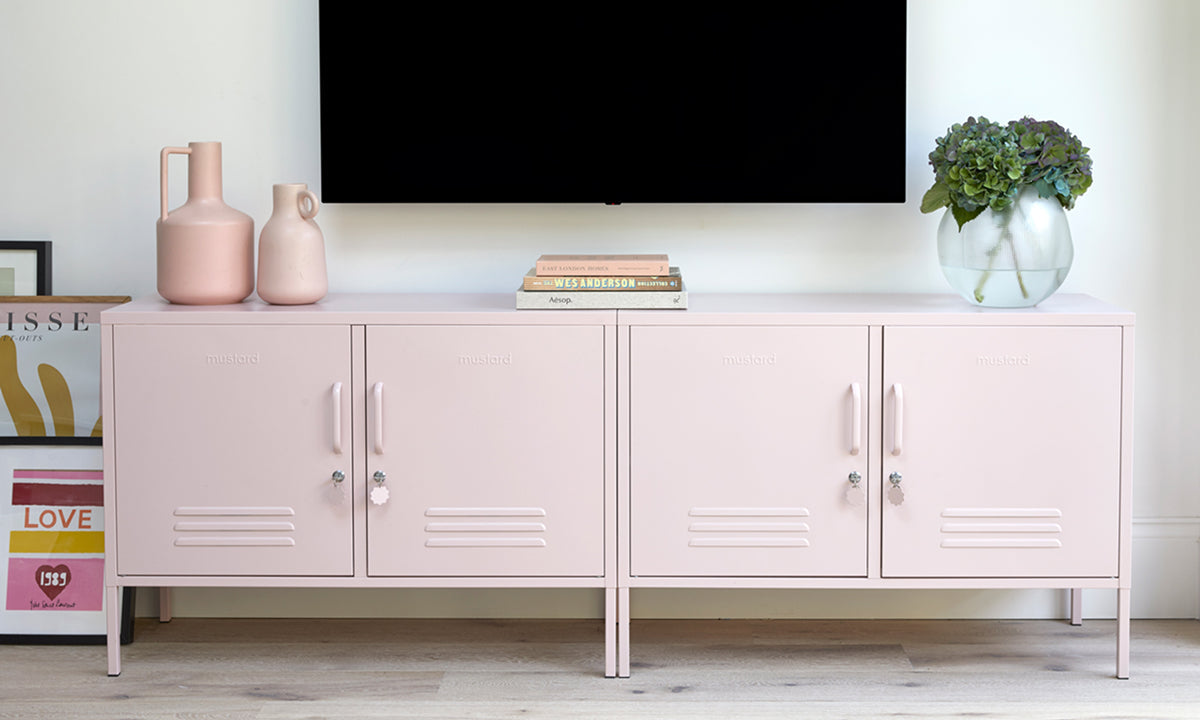 A pair of The Lowdown lockers in Blush pale pink beneath a wall-mounted TV, styled with vases, books and a leafy plant