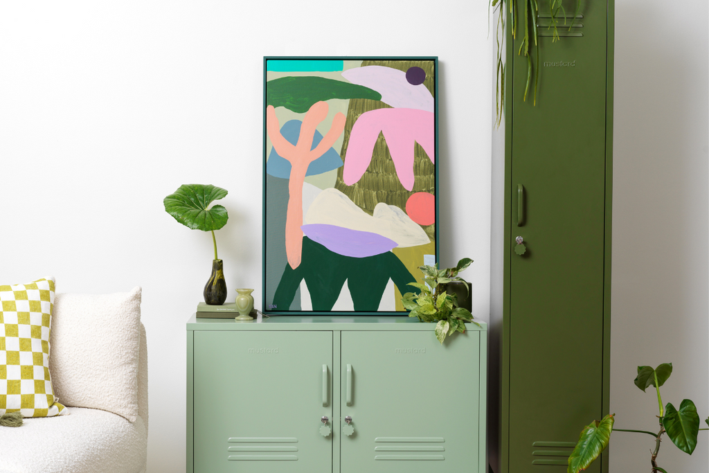 A brightly coloured print sits on top of a Sage Lowdown locker in a room filled with plants.