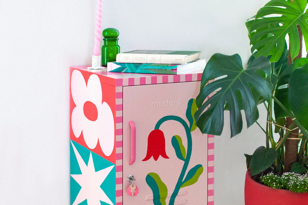 A Blush Shorty has been painted with a detailed floral design, with the edges in a pink checkerboard pattern. There is a monstera plant in a red pot beside it.